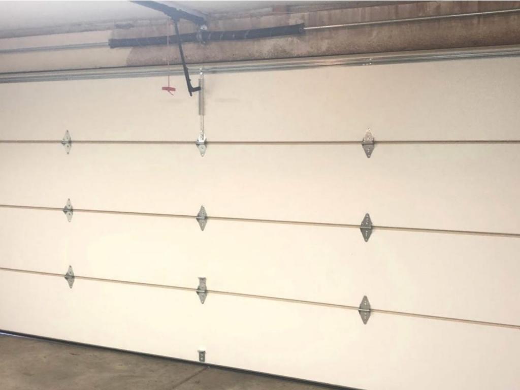 Residential garage door maintenance inspection showing sectional door panels, hinges, tracks, and hardware