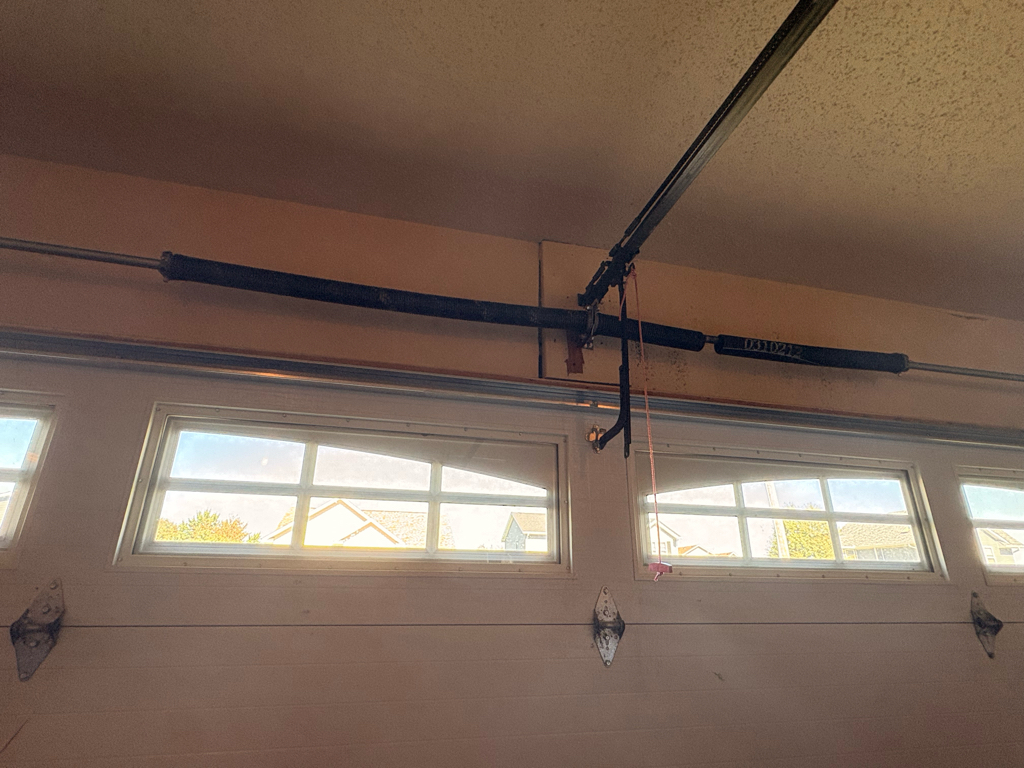 Garage door spring replacement in Council Bluffs, IA, showing the broken torsion spring system, center hardware, opener rail, and upper garage door components.